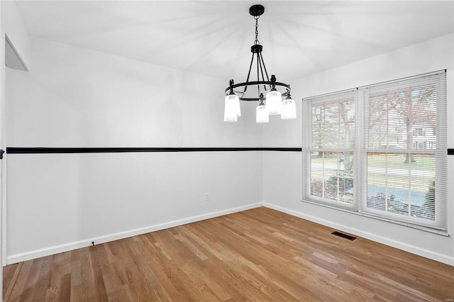 unfurnished dining area with wood-type flooring and an inviting chandelier