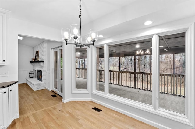 unfurnished dining area featuring a brick fireplace, light hardwood / wood-style flooring, and an inviting chandelier