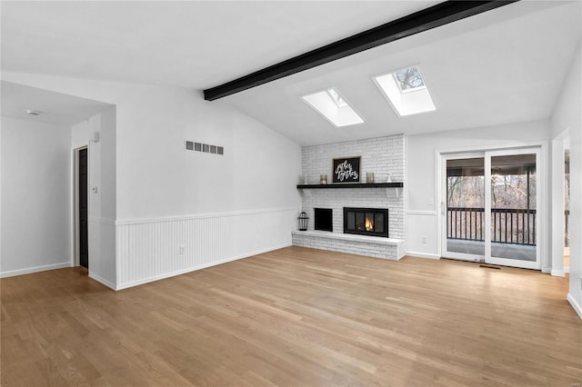 unfurnished living room featuring lofted ceiling with skylight, light hardwood / wood-style floors, and a brick fireplace