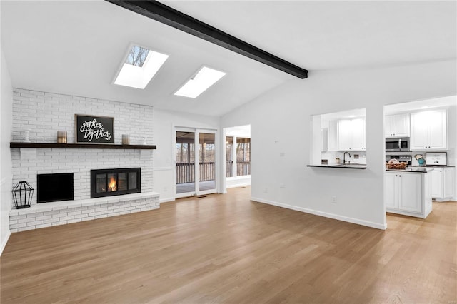 unfurnished living room featuring light hardwood / wood-style floors, sink, lofted ceiling with skylight, and a fireplace