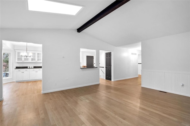 unfurnished living room featuring an inviting chandelier, lofted ceiling with beams, and light hardwood / wood-style floors