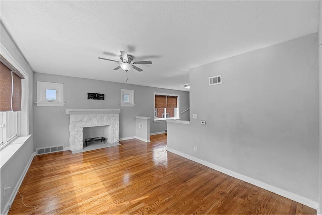 unfurnished living room featuring a wealth of natural light, ceiling fan, a fireplace, and wood-type flooring