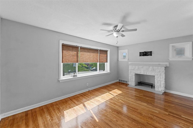 unfurnished living room featuring hardwood / wood-style flooring, ceiling fan, a stone fireplace, and a textured ceiling