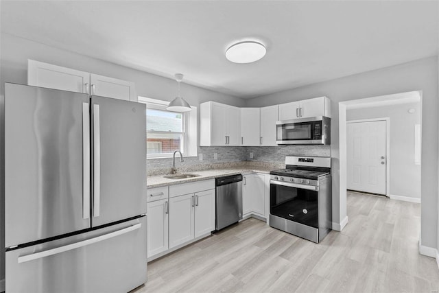 kitchen with sink, stainless steel appliances, decorative light fixtures, white cabinets, and light wood-type flooring