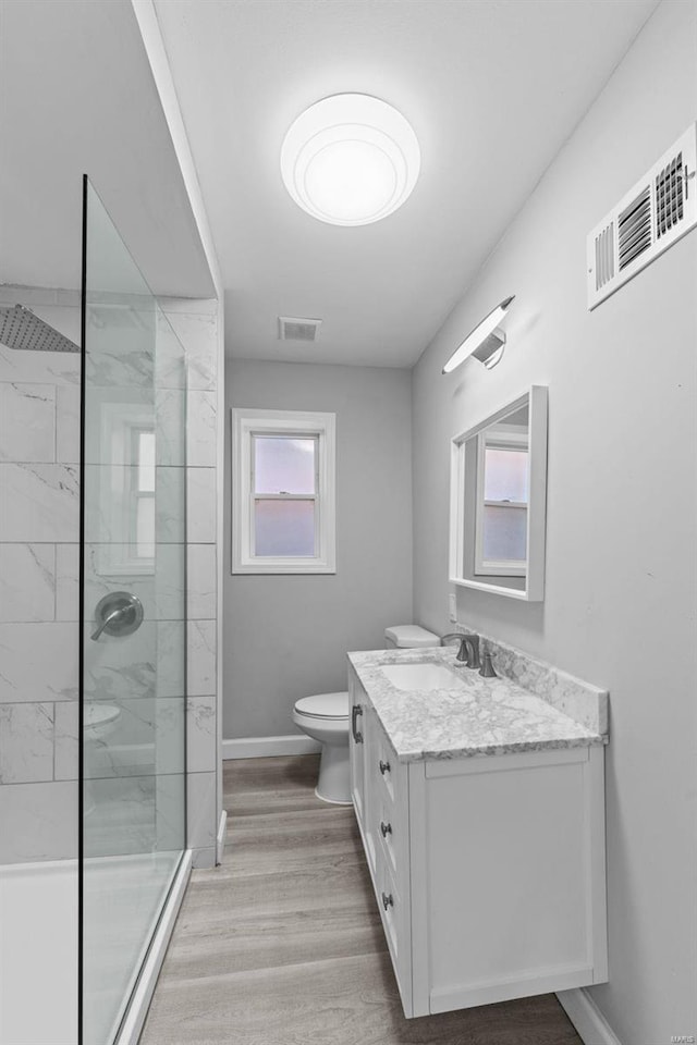 bathroom featuring a tile shower, vanity, wood-type flooring, and toilet