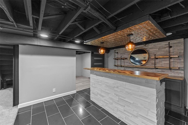 bar with hanging light fixtures, dark tile patterned flooring, and wood counters