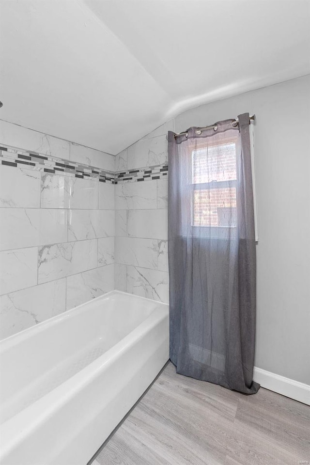 bathroom featuring hardwood / wood-style floors, tiled shower / bath combo, and vaulted ceiling