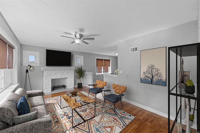 living room with hardwood / wood-style flooring, a stone fireplace, and ceiling fan