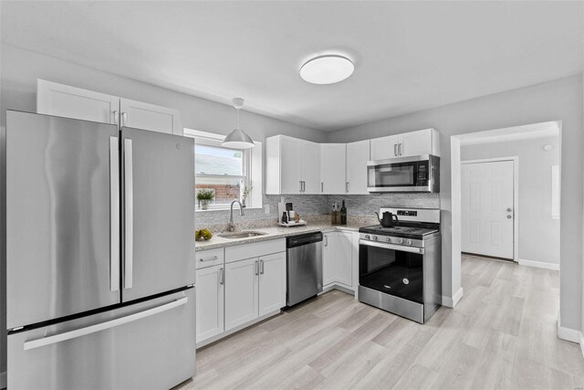 kitchen with sink, white cabinetry, backsplash, hanging light fixtures, and stainless steel appliances