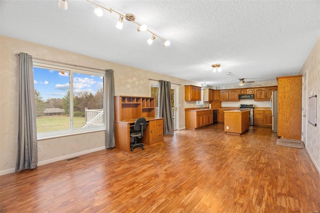 unfurnished living room with a textured ceiling, wood finished floors, visible vents, and baseboards