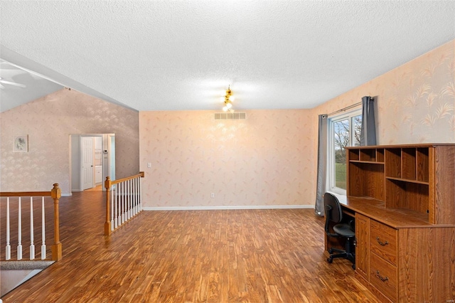 unfurnished office with a textured ceiling, wood finished floors, visible vents, and wallpapered walls