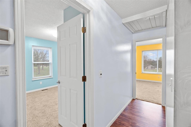 hallway with a textured ceiling, carpet flooring, baseboards, and visible vents