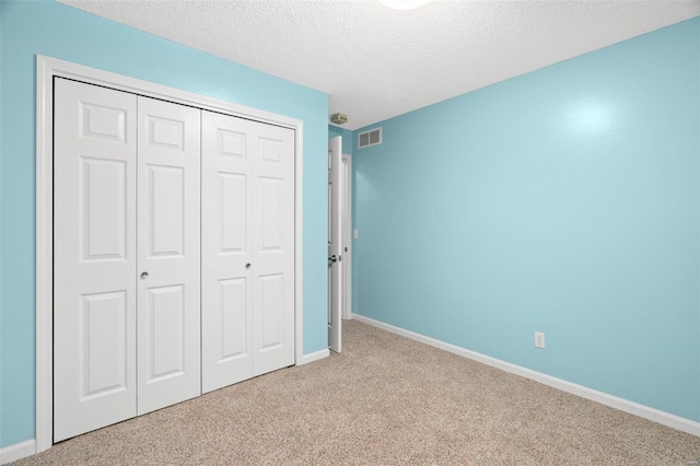 unfurnished bedroom with a textured ceiling, a closet, carpet, baseboards, and visible vents