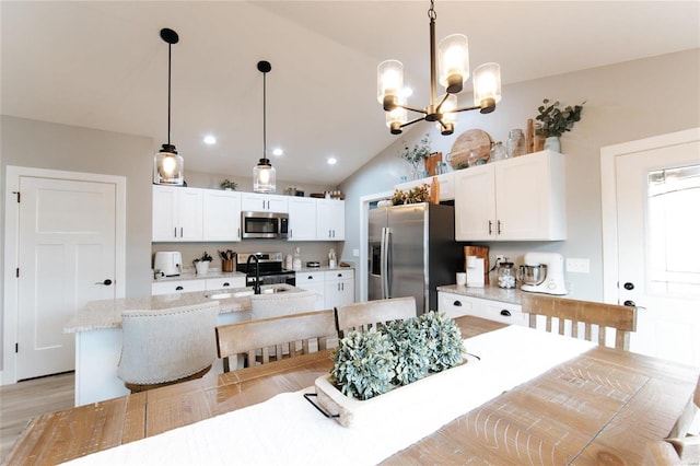 kitchen with stainless steel appliances, a kitchen island with sink, decorative light fixtures, white cabinets, and lofted ceiling