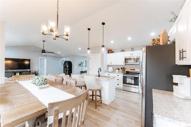 dining space featuring ceiling fan with notable chandelier, light hardwood / wood-style flooring, lofted ceiling, and sink