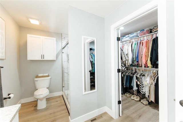 bathroom with hardwood / wood-style floors, an enclosed shower, and toilet