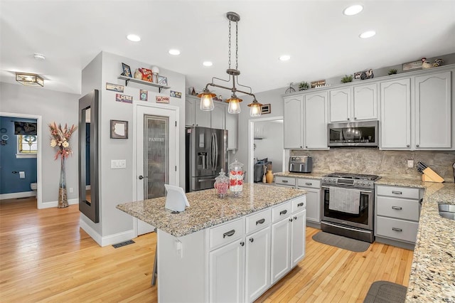 kitchen featuring stainless steel appliances, a center island, tasteful backsplash, light stone countertops, and pendant lighting