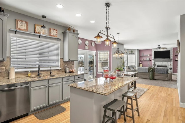 kitchen featuring sink, a fireplace, stainless steel dishwasher, a kitchen island, and pendant lighting