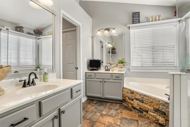 bathroom with lofted ceiling, tiled bath, and vanity