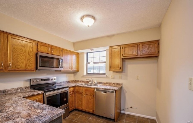 kitchen with a textured ceiling, sink, stainless steel appliances, and dark tile patterned flooring