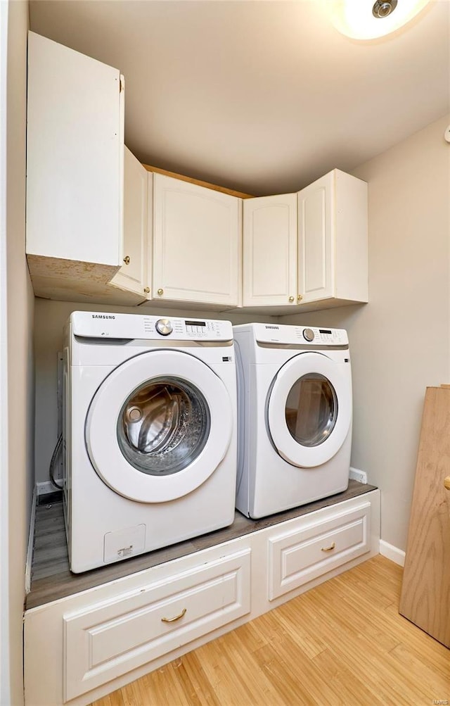 laundry area featuring washing machine and dryer, light hardwood / wood-style flooring, and cabinets