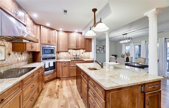 kitchen with appliances with stainless steel finishes, decorative columns, sink, decorative light fixtures, and an island with sink