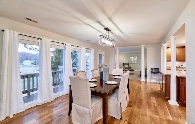 dining space featuring an inviting chandelier, light wood-type flooring, and decorative columns