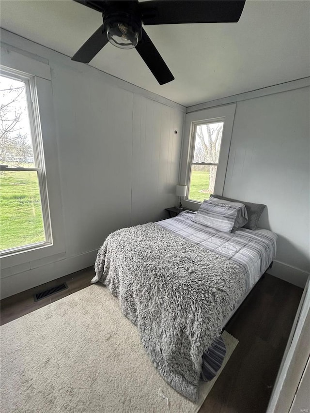 bedroom featuring ceiling fan, dark wood-type flooring, and multiple windows