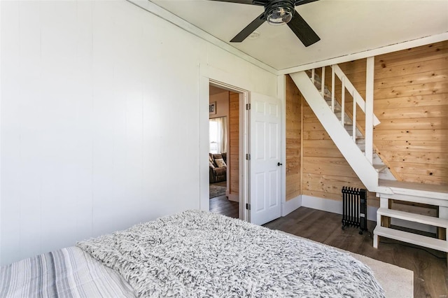 bedroom with ceiling fan, wooden walls, and dark hardwood / wood-style floors