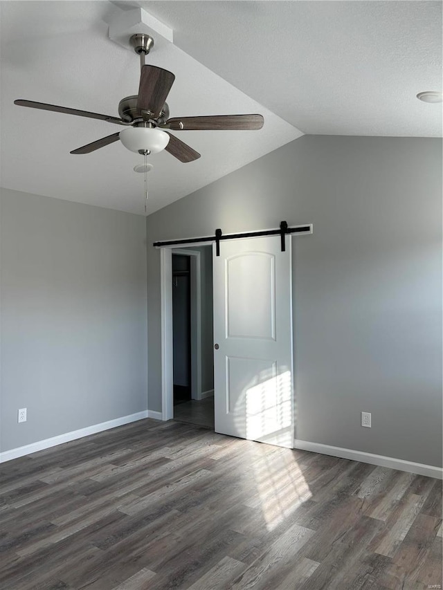 unfurnished bedroom featuring a barn door, dark hardwood / wood-style floors, vaulted ceiling, and ceiling fan