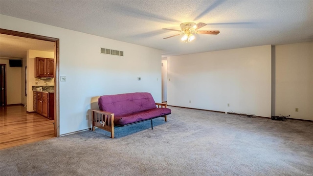 living area with light carpet, ceiling fan, and a textured ceiling