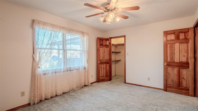 unfurnished bedroom featuring light carpet, a walk in closet, ceiling fan, a textured ceiling, and a closet