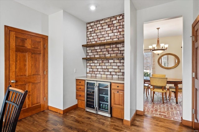 bar featuring baseboards, beverage cooler, a chandelier, dark wood finished floors, and a bar