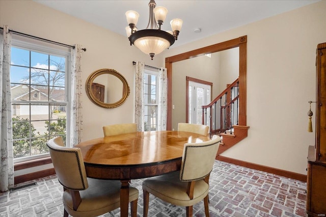 dining area featuring visible vents, a notable chandelier, brick floor, baseboards, and stairs