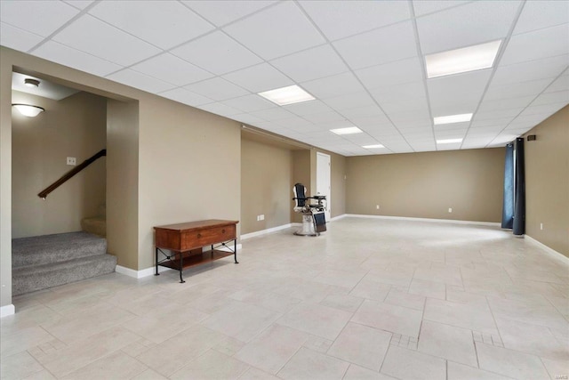 finished basement featuring stairs, a paneled ceiling, and baseboards