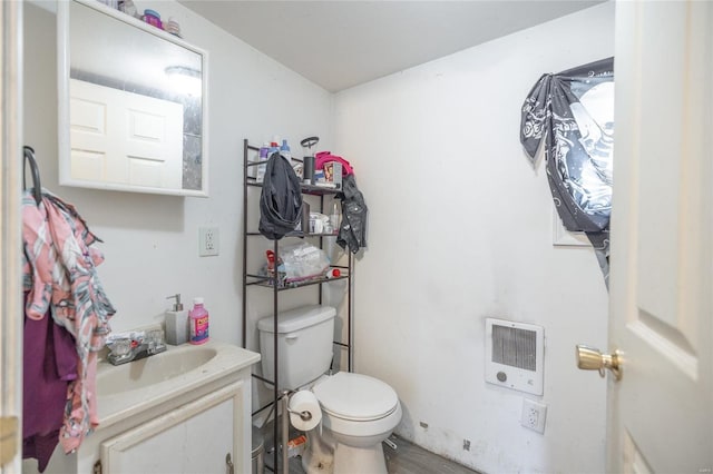 bathroom with wood-type flooring, vanity, heating unit, and toilet