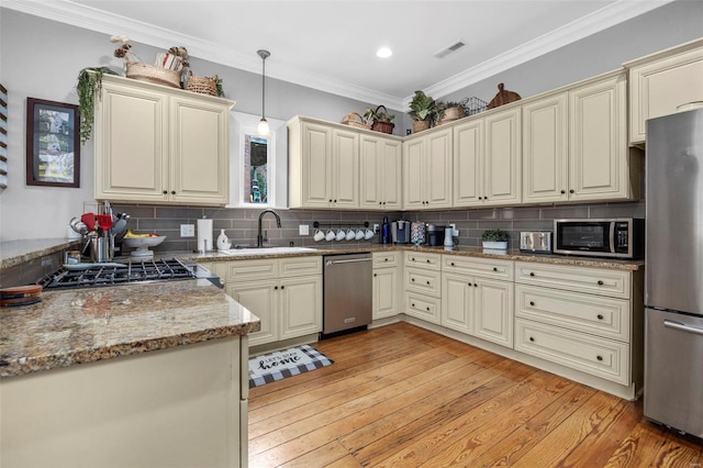 kitchen with sink, hanging light fixtures, stainless steel appliances, cream cabinetry, and light wood-type flooring