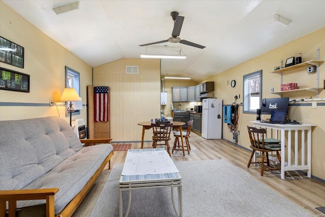 living room with ceiling fan, light hardwood / wood-style floors, and vaulted ceiling