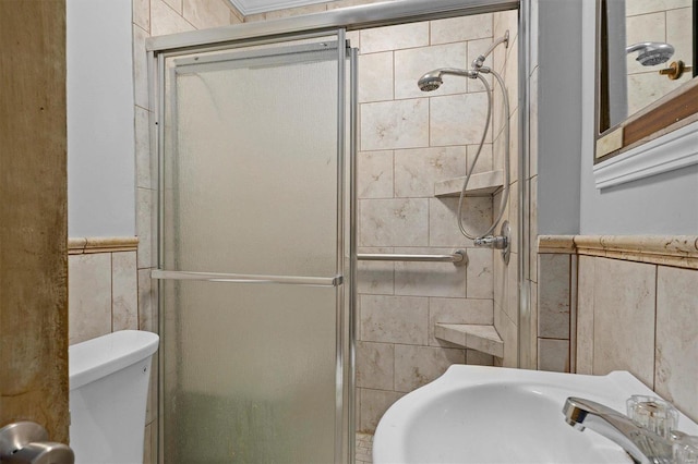 bathroom with sink, a shower with door, tile walls, and toilet