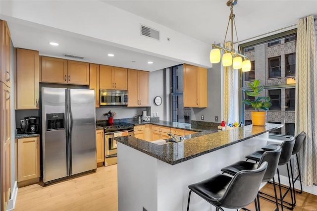 kitchen with kitchen peninsula, stainless steel appliances, decorative light fixtures, light hardwood / wood-style floors, and a breakfast bar area