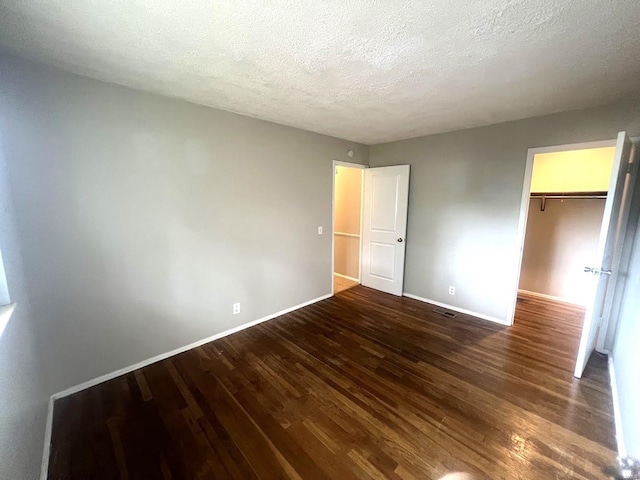 unfurnished bedroom featuring a textured ceiling, a spacious closet, dark wood-type flooring, and a closet