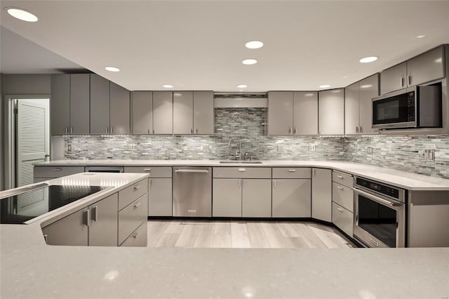 kitchen with gray cabinetry, sink, decorative backsplash, light wood-type flooring, and appliances with stainless steel finishes