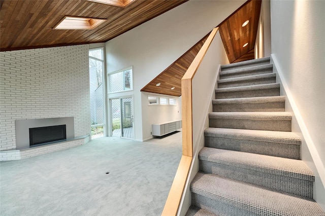 staircase with carpet, wooden ceiling, high vaulted ceiling, a skylight, and a fireplace