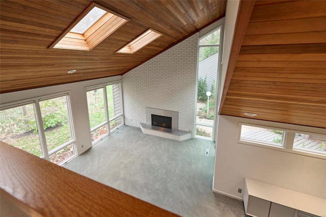 unfurnished living room featuring a healthy amount of sunlight, wooden ceiling, lofted ceiling with skylight, and a brick fireplace