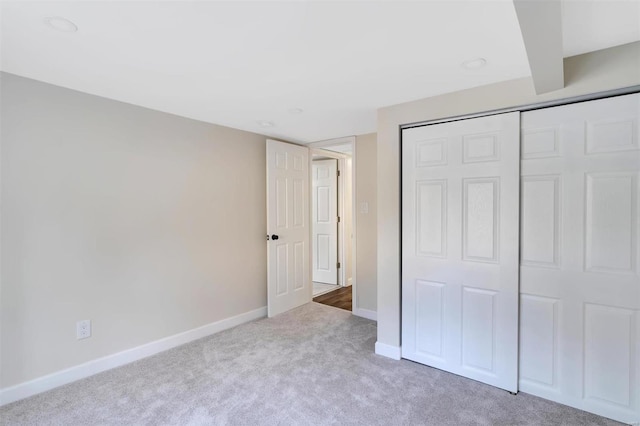 unfurnished bedroom featuring light carpet, a closet, and beamed ceiling