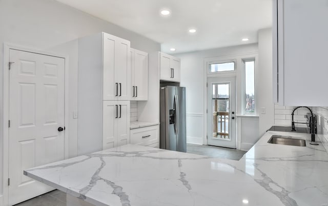 kitchen featuring sink, white cabinetry, light stone counters, stainless steel fridge with ice dispenser, and backsplash