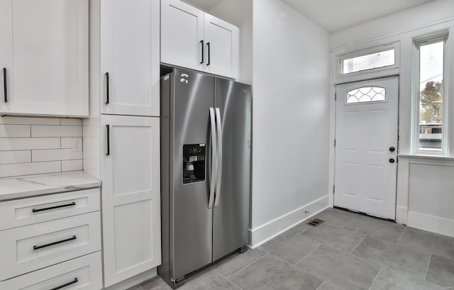 kitchen with tasteful backsplash, stainless steel refrigerator with ice dispenser, light stone countertops, and white cabinets