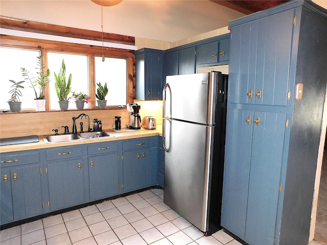 kitchen with blue cabinetry, stainless steel fridge, light tile patterned flooring, and sink