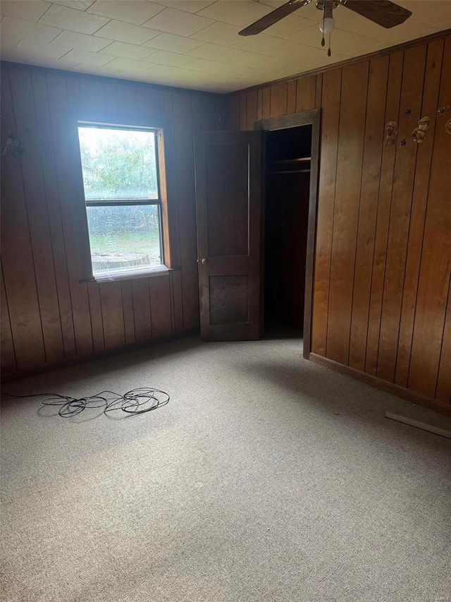 unfurnished room with carpet, ceiling fan, and wooden walls