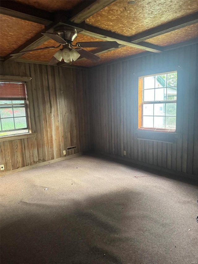 carpeted empty room featuring beamed ceiling, ceiling fan, and wooden walls